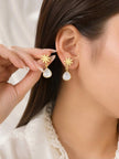 Gold-plated snowflake stud drop earrings worn on a woman's ear with white milky teardrop pendants dangling