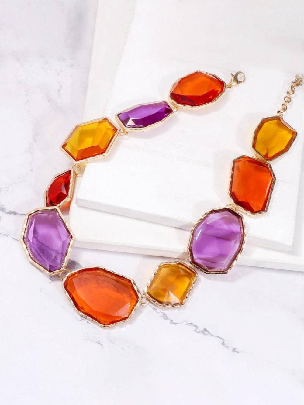 Gold-tone multicolour choker necklace laid flat on white marble showing full stone arrangement and clasp