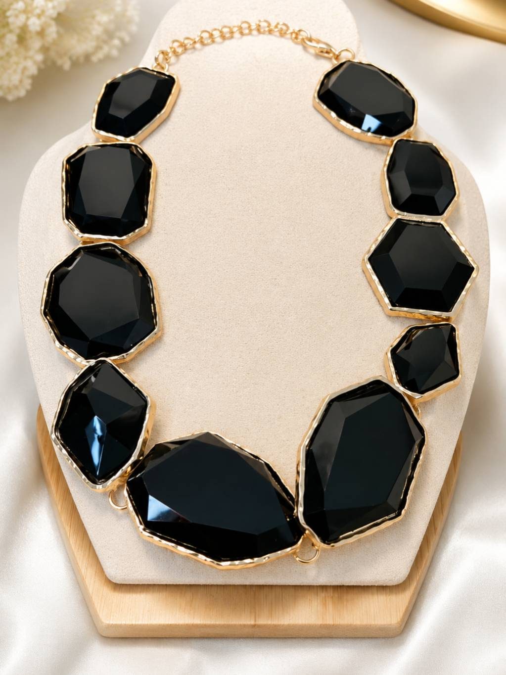 Gold-tone black faceted stone statement necklace displayed on a cream velvet jewellery bust