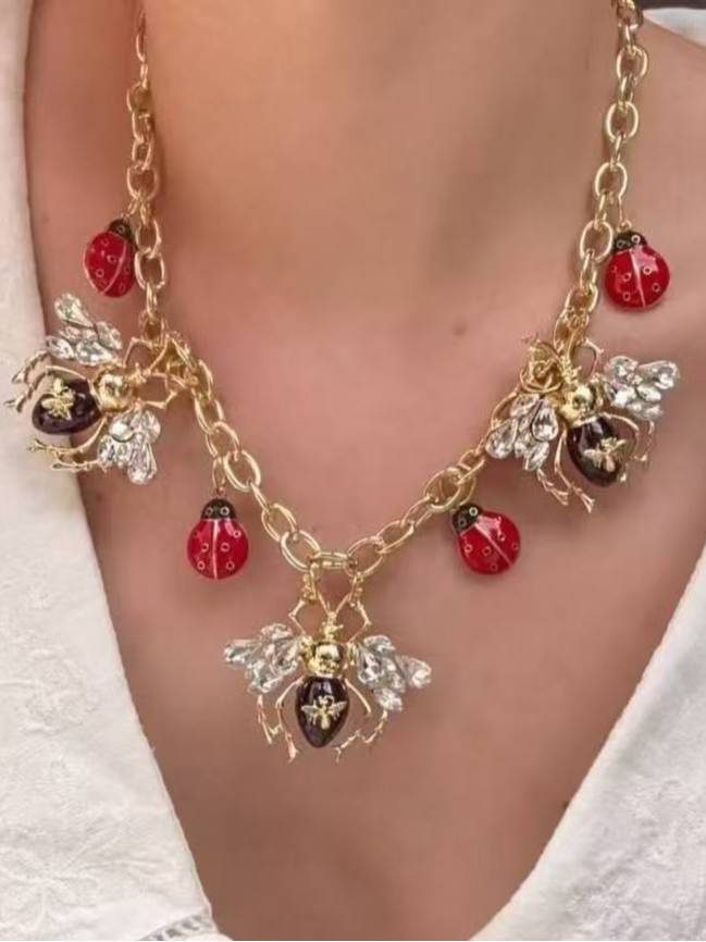 Close-up of bee and ladybug charm necklace worn on model showing crystal bee detail at centre