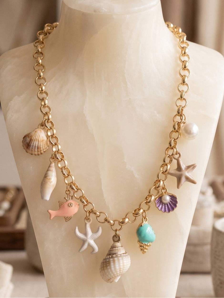 Gold-toned rolo chain necklace with shell, starfish, fish and conch charms displayed on a white marble jewellery bust