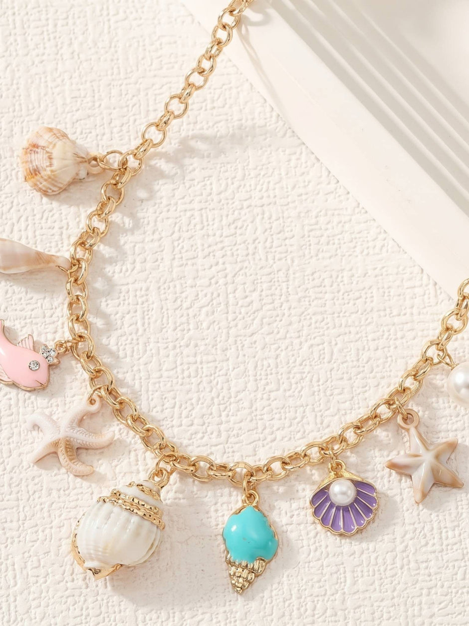 Close-up of ocean charm necklace showing turquoise conch, purple scallop shell with pearl, spiral shell and pink enamel fish charms