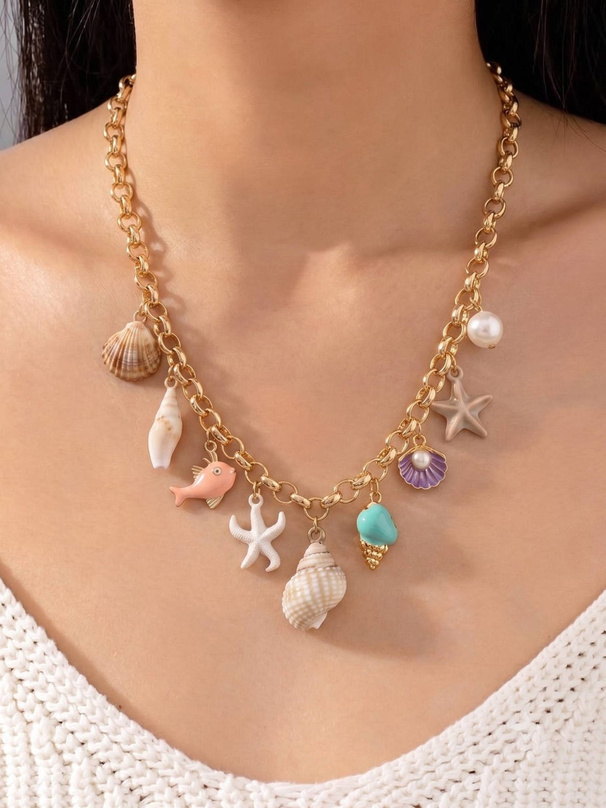 Ocean charm necklace worn around a woman's neck over a white knit top showing full charm arrangement