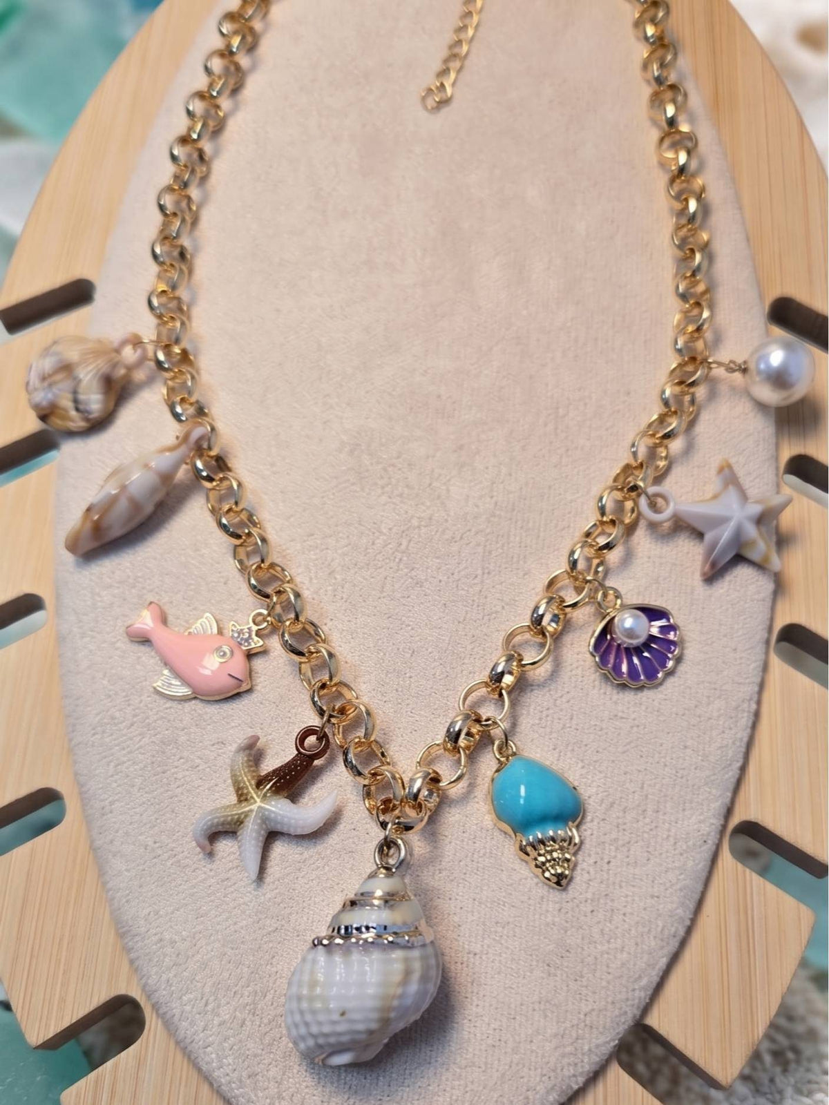 Gold-toned ocean charm necklace laid flat on a wooden display stand showing adjustable extension chain at the back