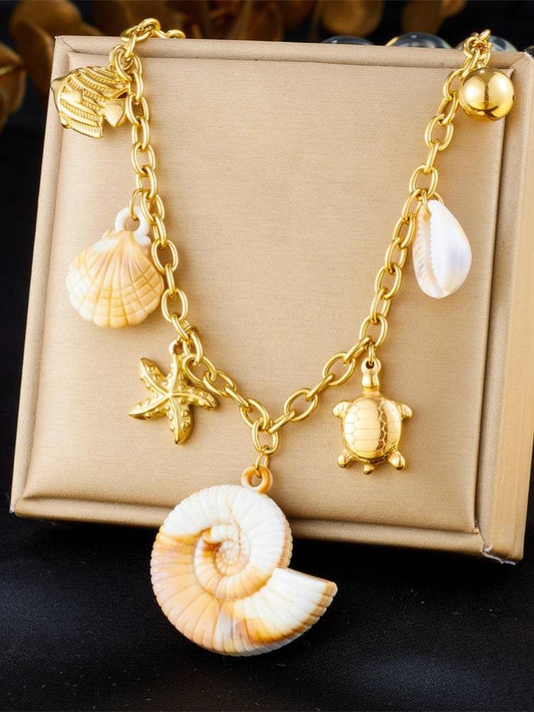 Close-up of ocean charm necklace in a beige jewellery box highlighting gold sea turtle, starfish and spiral shell pendant