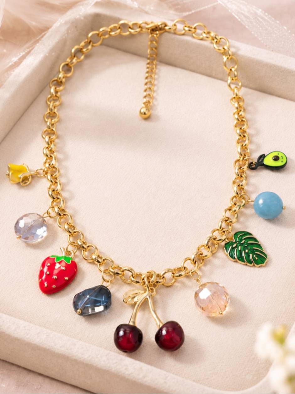Full view of fruit charm necklace laid flat on a beige velvet tray showing lobster clasp and extender chain