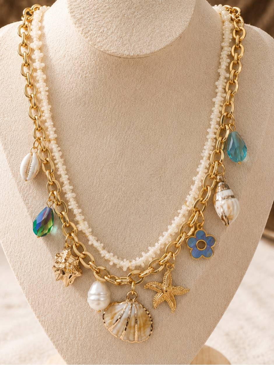 Gold-toned layered charm necklace with shell, starfish and crystal pendants displayed on a cream jewellery bust
