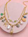Close-up flat lay of gold charm necklace with conch shell, starfish, pearl and crystal pendants on pink surface