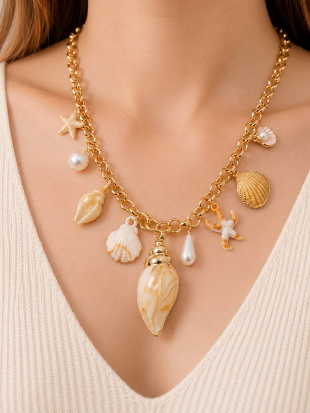 Model wearing gold-plated seashell charm necklace over a cream ribbed v-neck top showing full charm arrangement