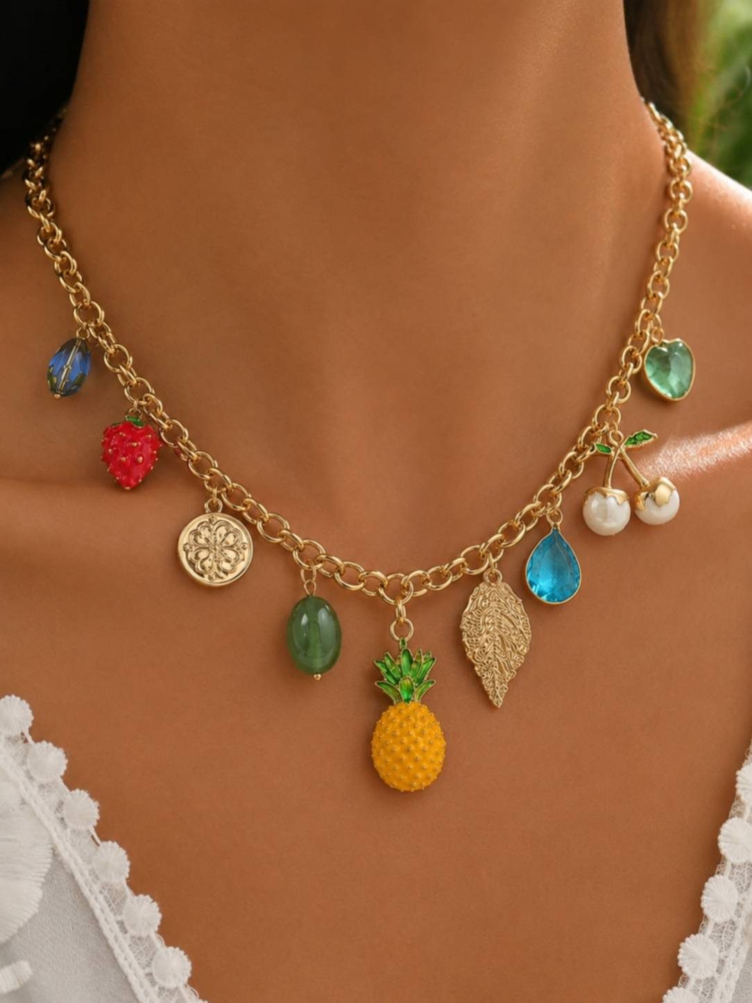 Fruit charm necklace worn around a woman's neck over a white lace top showing scale and styling
