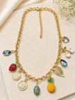 Full flat-lay of gold-toned fruit charm necklace on beige surface showing lobster clasp and extender chain detail