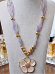 Gold-tone shell flower pendant necklace displayed on a grey jewellery bust against a neutral background