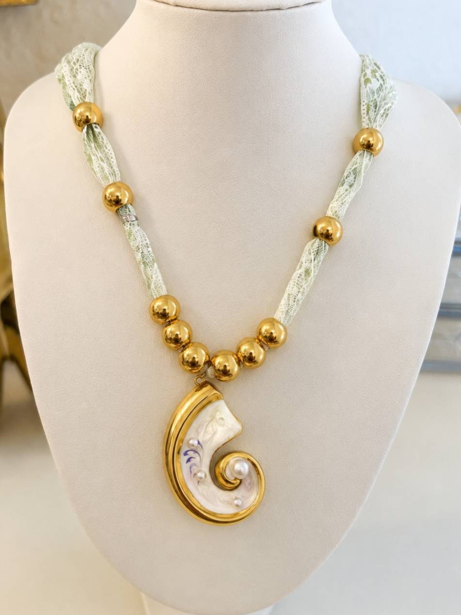 Gold-plated nautilus shell pendant necklace displayed on a cream jewellery bust, showing lace chain and gold bead detailing