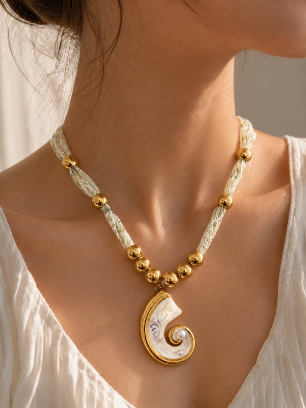Model wearing gold shell pendant necklace against collarbone, styled with a white off-shoulder top
