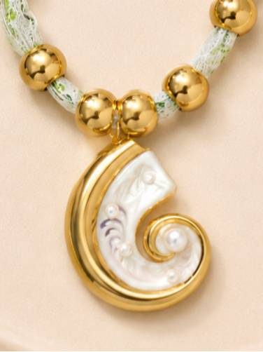 Close-up of nautilus shell pendant with mother-of-pearl inlay, faux pearl accents and gold-tone frame against gold beads