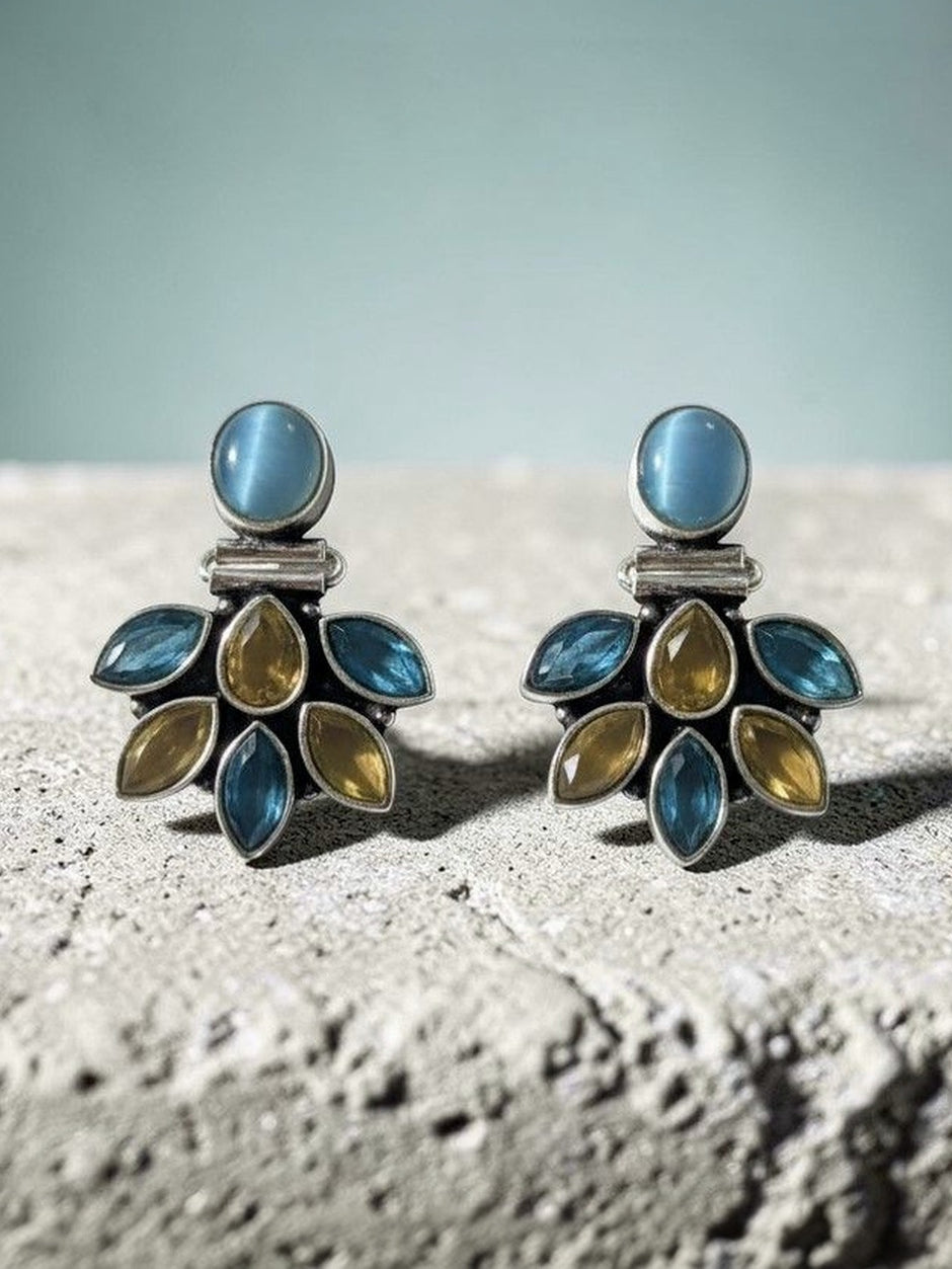Pair of oxidised silver studs with blue cat-eye top and teal and citrine stone fan cluster, displayed on textured stone surface