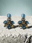 Pair of oxidised silver studs with blue cat-eye top and teal and citrine stone fan cluster, displayed on textured stone surface