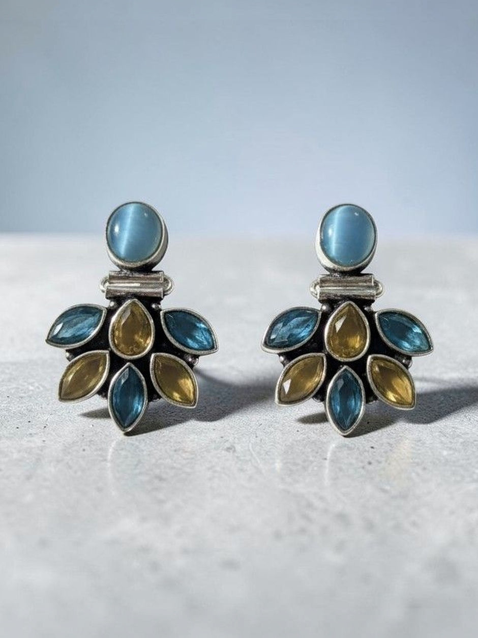 Close-up of oxidised silver blue and citrine stone cluster stud earrings resting on grey stone surface with soft background