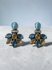 Close-up of oxidised silver blue and citrine stone cluster stud earrings resting on grey stone surface with soft background