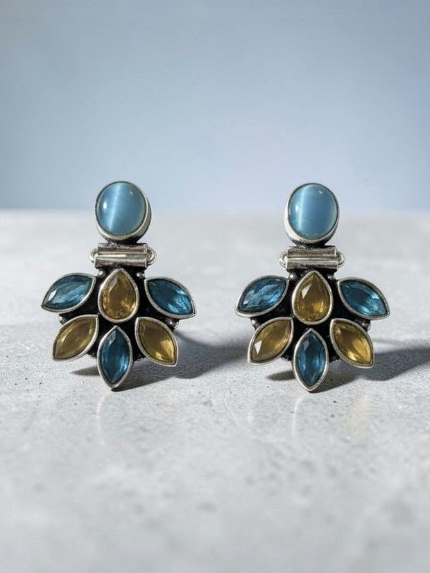 Close-up of oxidised silver blue and citrine stone cluster stud earrings resting on grey stone surface with soft background