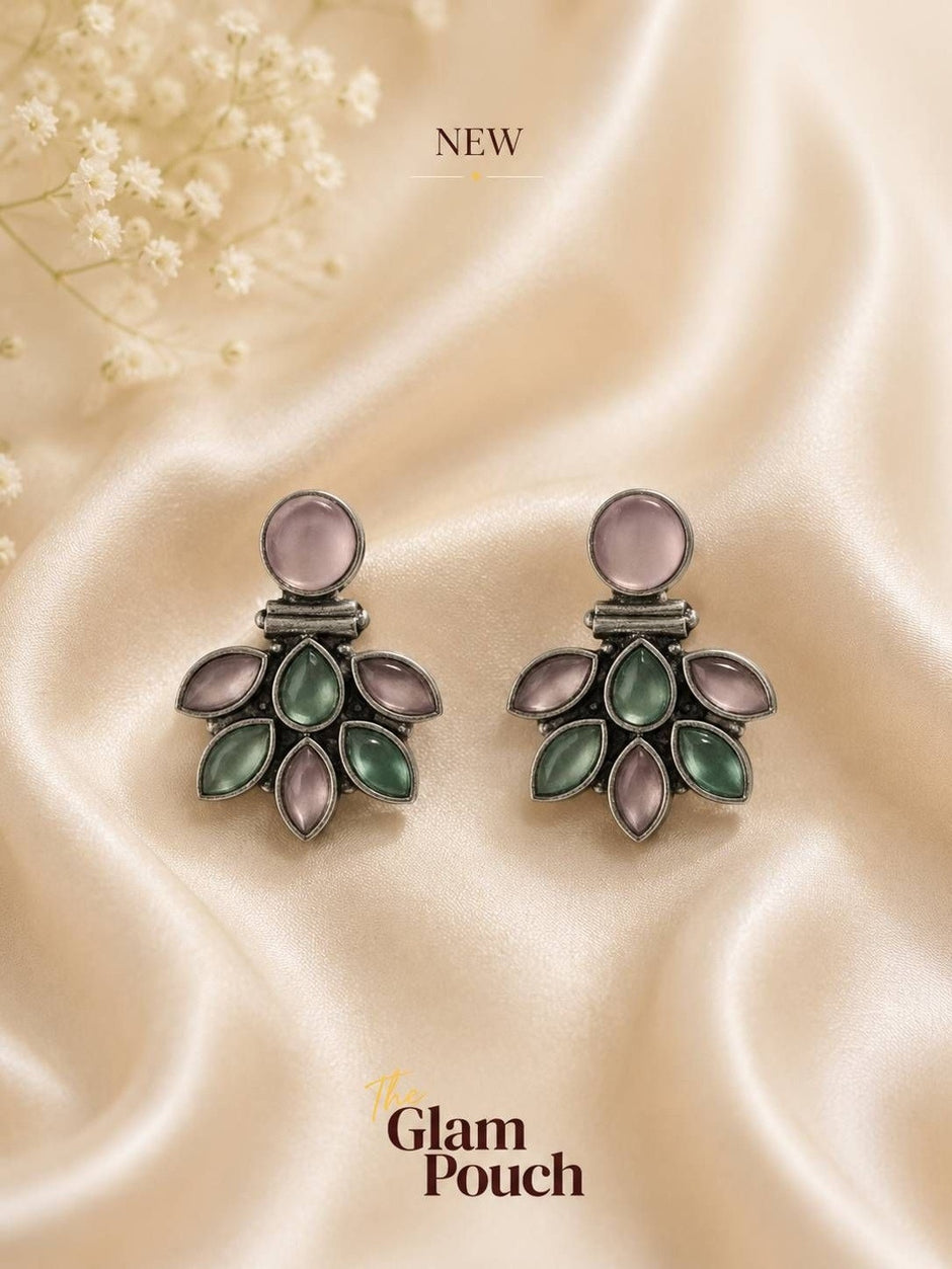 Pair of oxidised silver floral stud earrings with pink and jade-tone stones on cream satin fabric