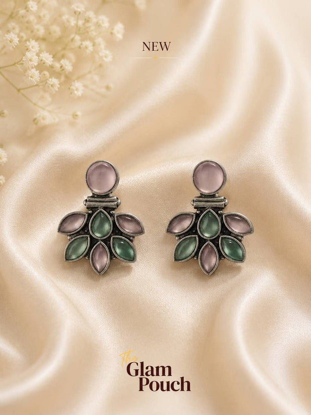 Pair of oxidised silver floral stud earrings with pink and jade-tone stones on cream satin fabric