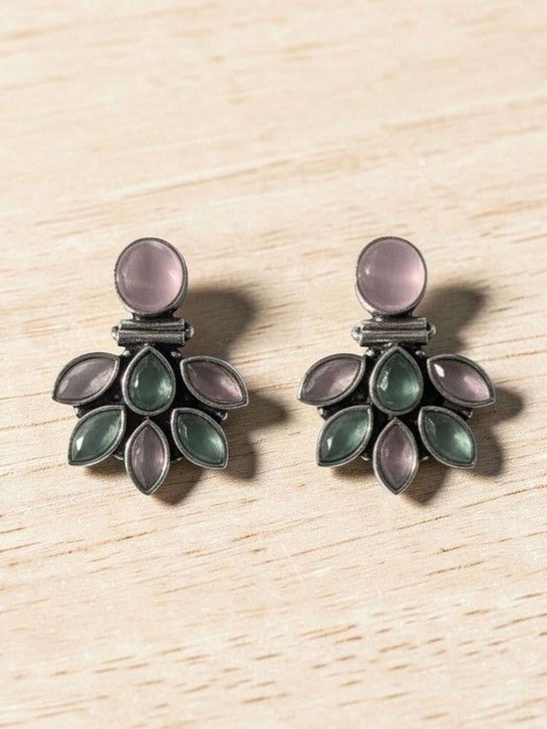 Close-up of oxidised silver floral earrings showing marquise pink and green stone petal arrangement on wood surface