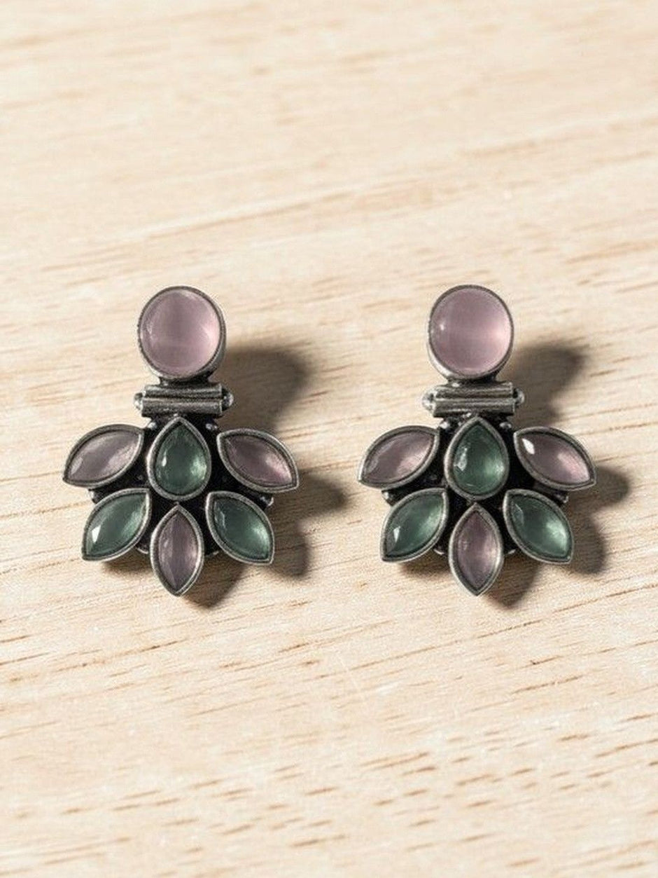 Close-up of oxidised silver floral earrings showing marquise pink and green stone petal arrangement on wood surface