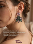 Woman wearing oxidised silver floral stud earring with pink cabochon top and jade-tone petal cluster