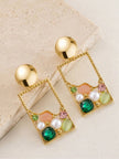 Pair of gold-plated rectangle drop earrings with green crystals, faux pearls and pink enamel on a beige stone surface