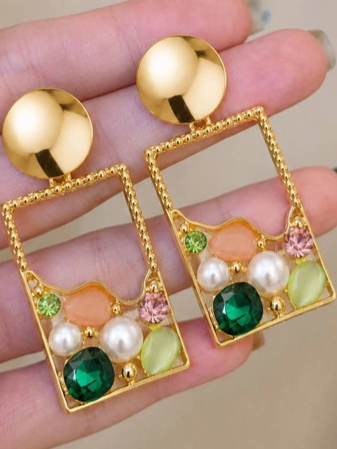 Close-up of both gold rectangle drop earrings held in an open palm showing crystal and pearl detail