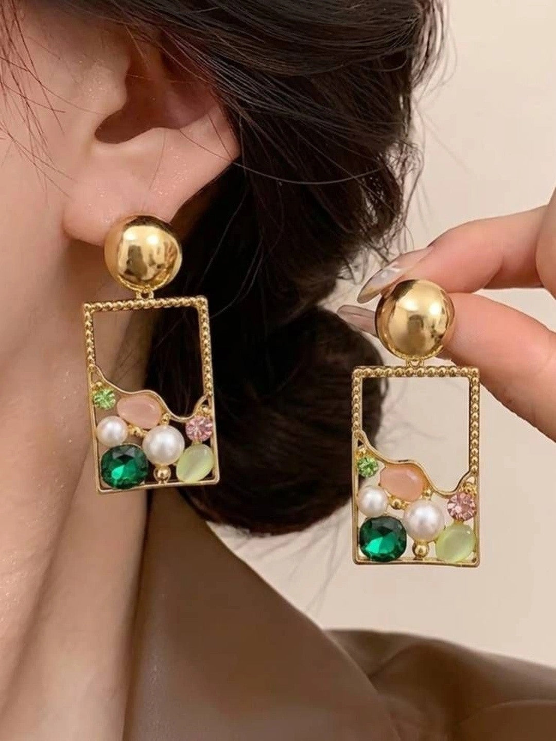 Model wearing one gold rectangle drop earring while holding the second earring up beside it