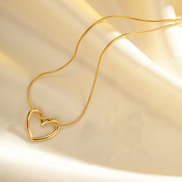 A gold-colored hollow heart pendant necklace laid out on a flat surface with a soft light source creating gentle shadows.
