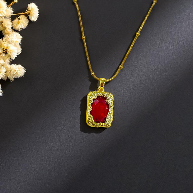 Gold plated necklace with red gemstone pendant on black background – Glampouch jewelry
