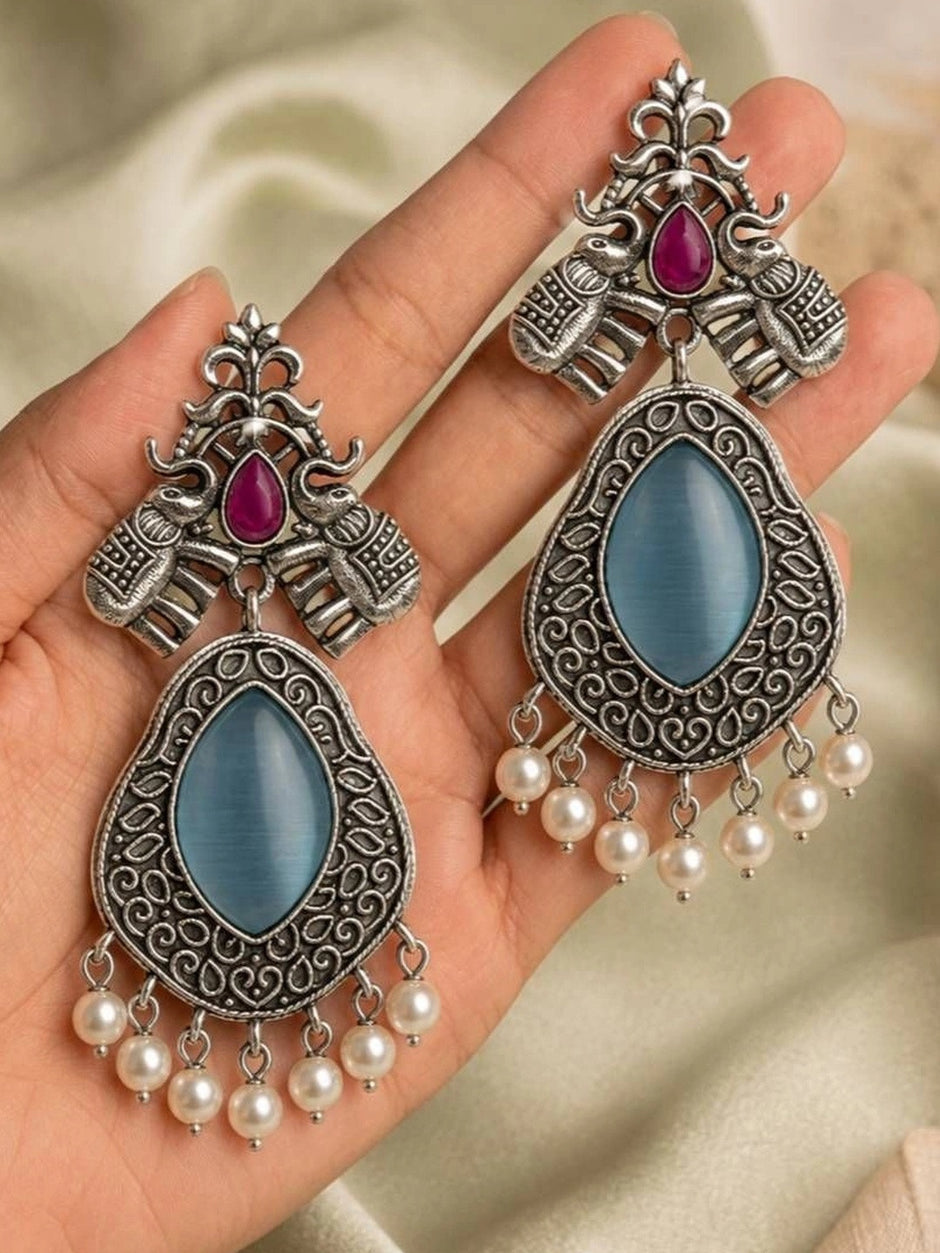 Two oxidised silver elephant teardrop earrings held in an open palm showing scale and blue cat-eye stone detail