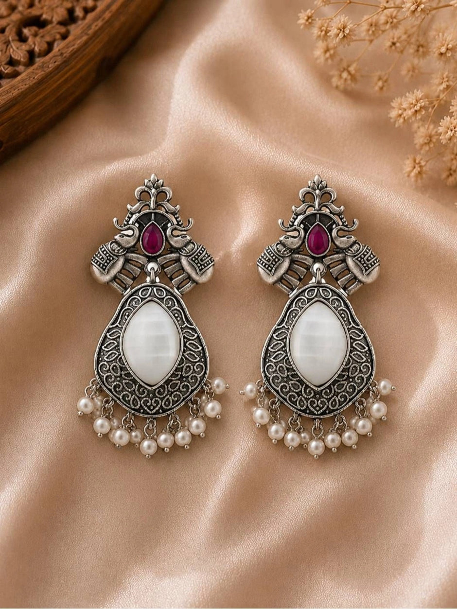 Pair of oxidised silver elephant chandbali earrings with white stone and pearl drops on satin fabric