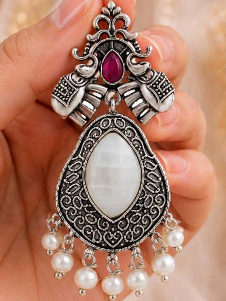 Close-up of oxidised silver chandbali earring showing elephant motif, red stone and filigree teardrop pendant held in hand