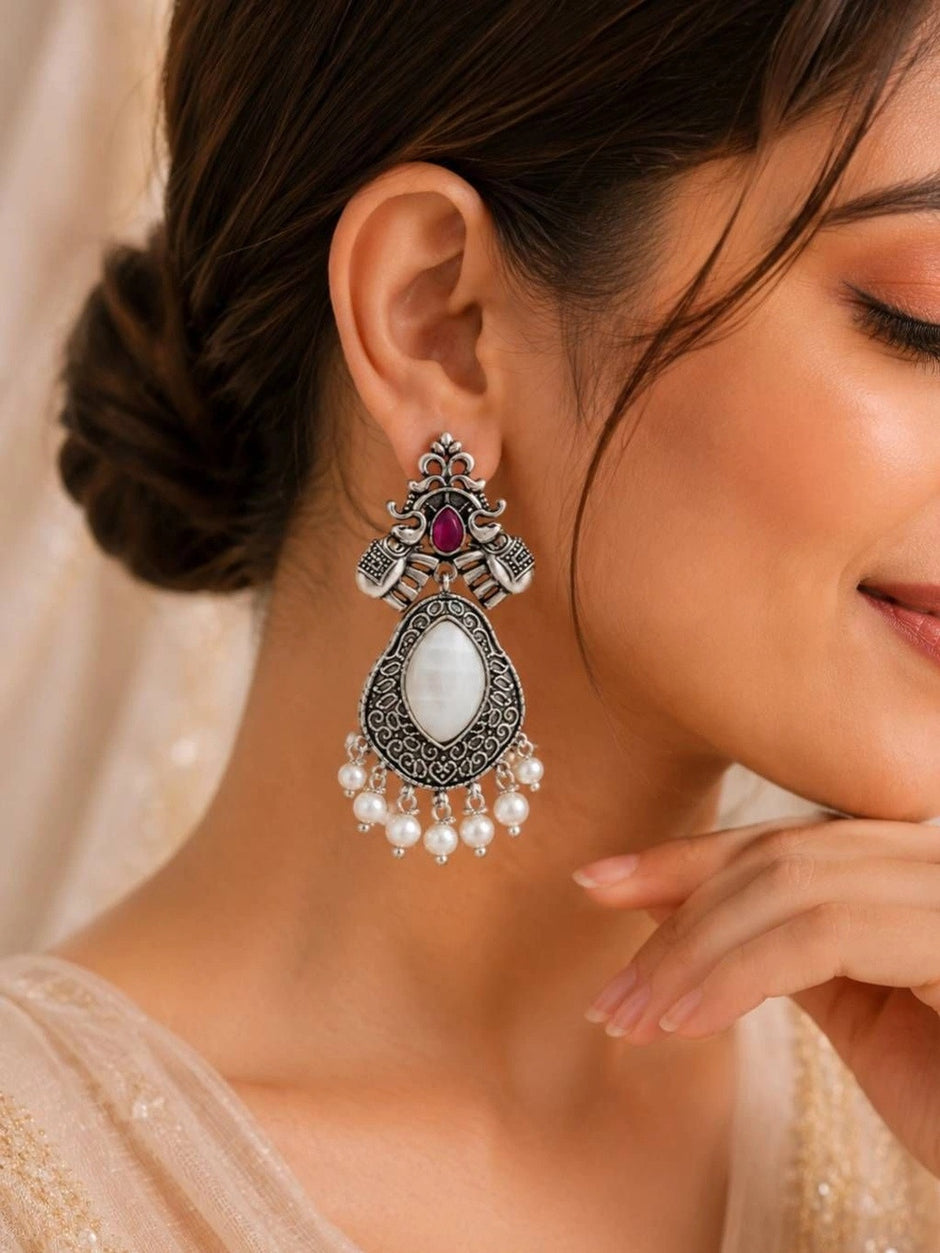 Side profile of woman wearing oxidised silver elephant chandbali earring with pearl fringe against light background