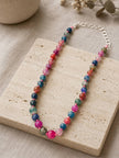 Vibrant multicolour beaded necklace resting on a travertine tile with dried eucalyptus in the background
