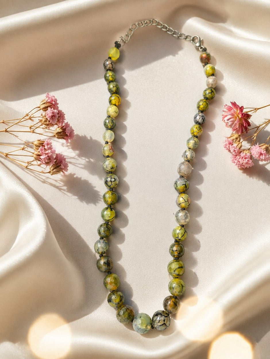Dragon vein agate bead necklace laid flat on ivory satin fabric with pink dried flowers