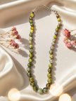 Dragon vein agate bead necklace laid flat on ivory satin fabric with pink dried flowers