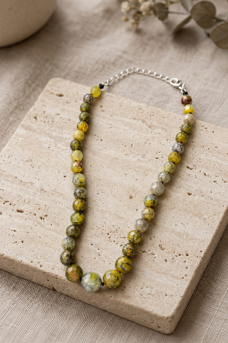 Green agate beaded necklace displayed on a textured travertine stone tile with dried eucalyptus