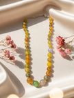 Multicolour faceted agate bead necklace laid flat on ivory satin with pink dried flowers