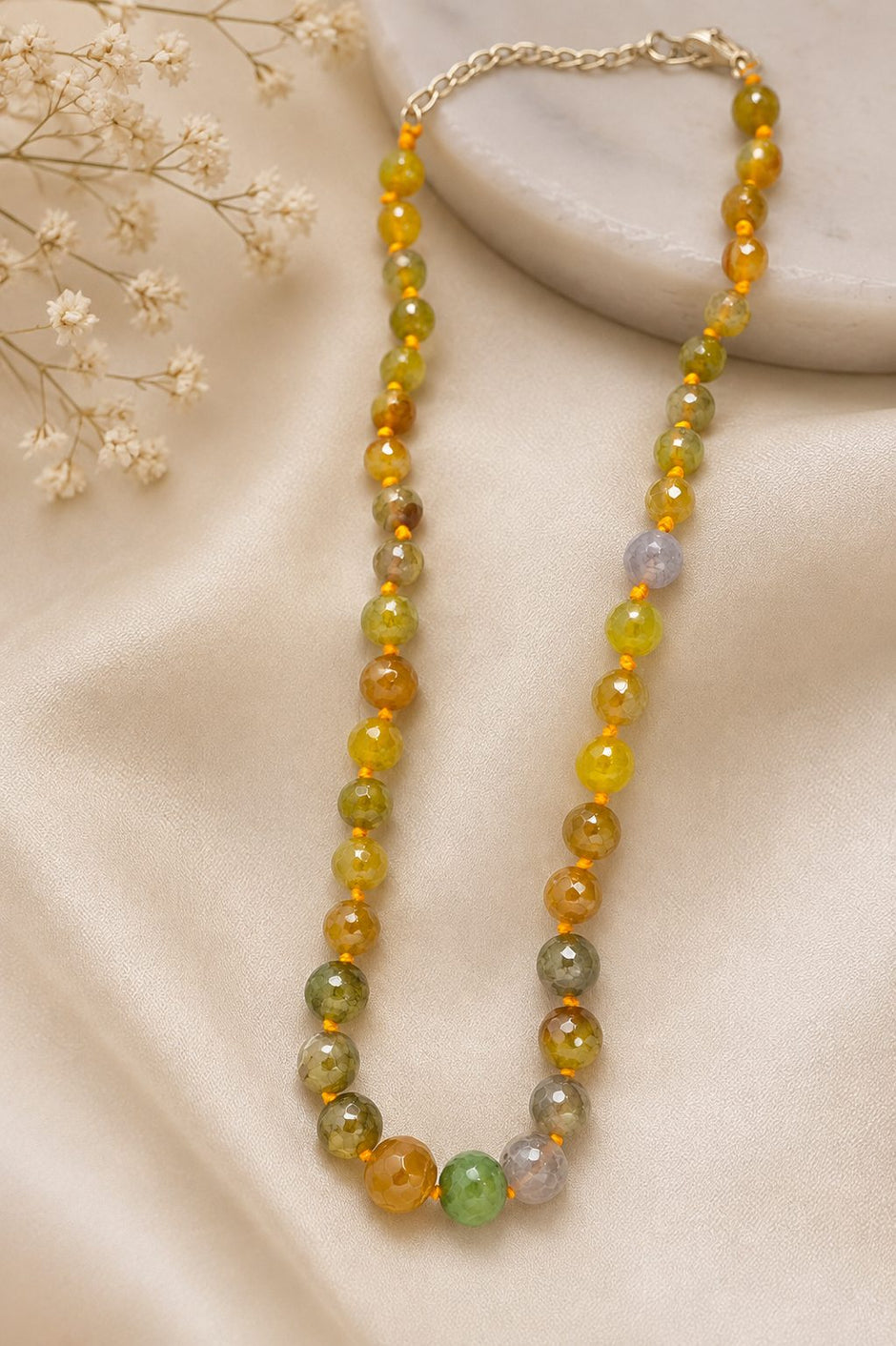 Faceted multicolour bead necklace with mint-green centre bead on a cream satin surface