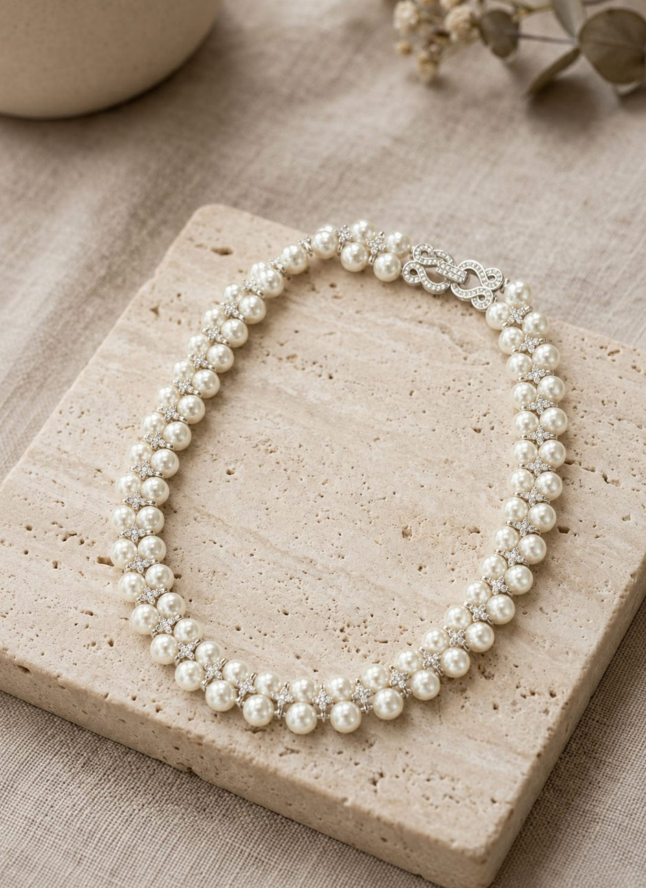 Pearl and crystal choker necklace displayed on a travertine stone tile with eucalyptus sprigs in background