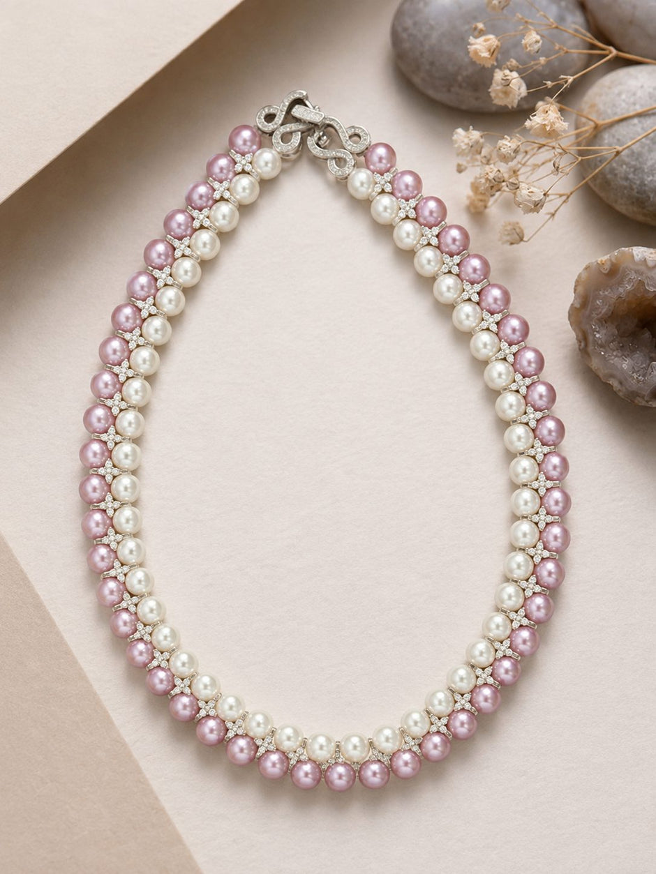 Overhead flat-lay of double-row pink and white pearl necklace on beige surface with stones and dried botanicals