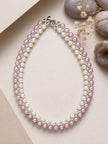 Overhead flat-lay of double-row pink and white pearl necklace on beige surface with stones and dried botanicals