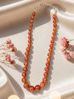 Graduated carnelian agate bead necklace laid flat on cream satin fabric with pink dried flowers