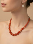 Model wearing carnelian bead necklace paired with silver and pearl drop earrings against a beige background