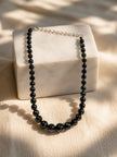 Black graduated bead necklace draped over a white marble block with silver extension chain visible in sunlight